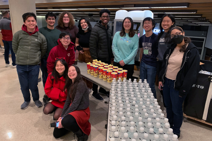 12 MIT students pose at the back of a lecture hall with a table full of popcorn and bottled water