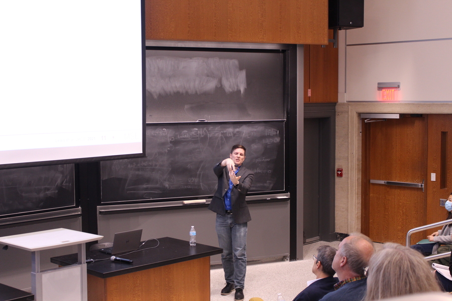 Robert Macfarlane gives a talk in a lecture hall with blackboard and screen in the background