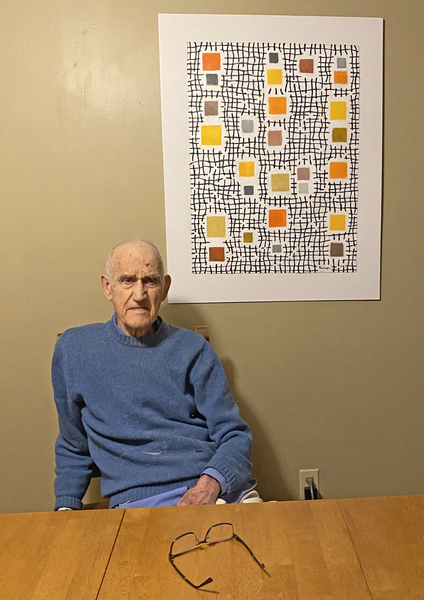 Robert Balluffi, seated, poses for a photo. A watercolor painting, of squares and crosshatched lines, hangs above his left shoulder.