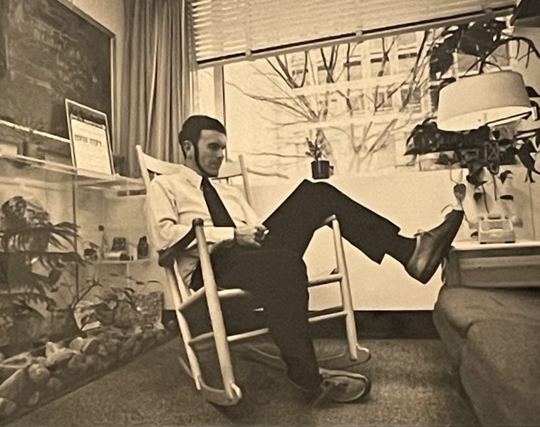 An old, sepia-toned photograph of Professor Richard Wurtman in his office in the 1980s. He is seated and leaning back in the chair with one foot up on a couch.
