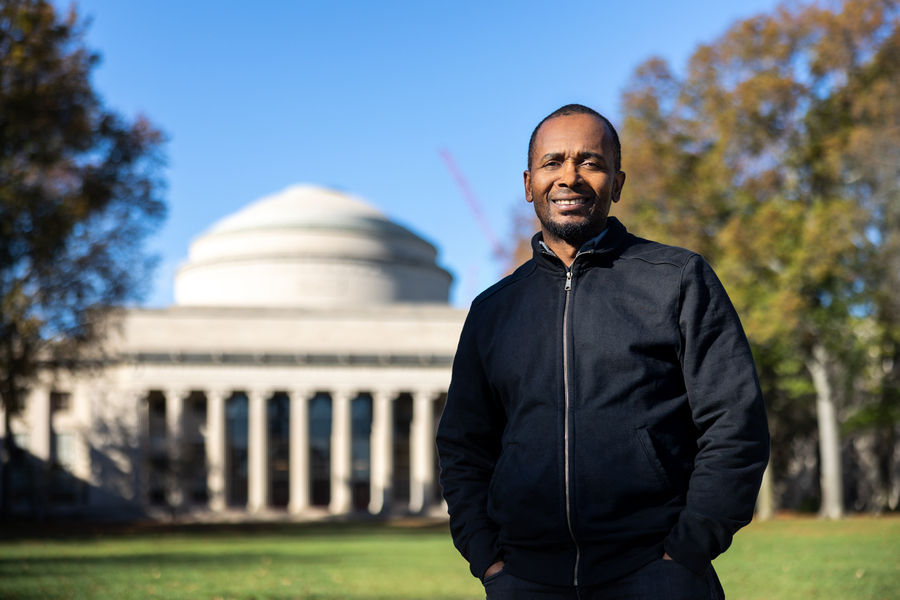 Brandon Ogbunu stands in black zip up jacket on Killian Court in front of the MIT Dome.