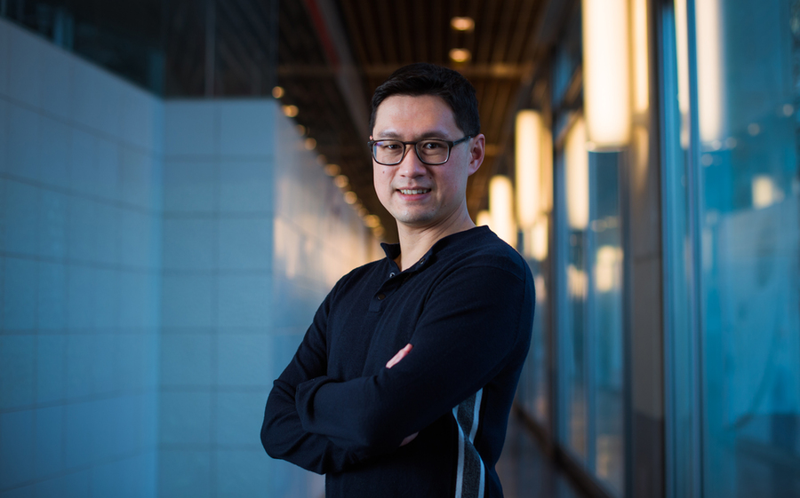Li, with arms crossed, stands in the middle of a hallway with blue-tinted light in background.