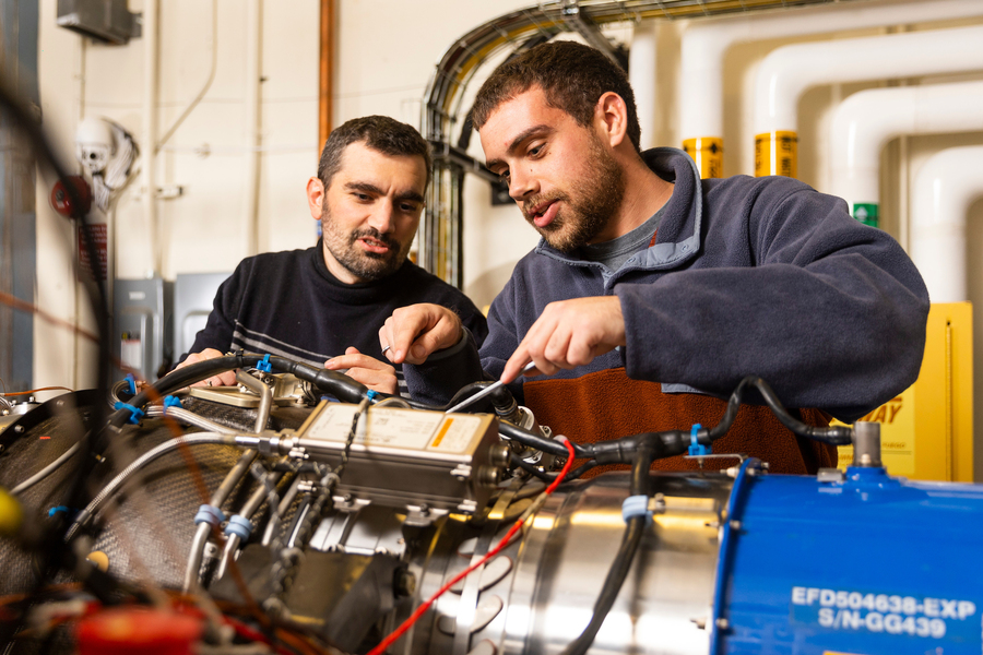 David Gonzalez Cuadrado and Joseph Chiapperi use a screwdriver to work on an engine in a laboratory.