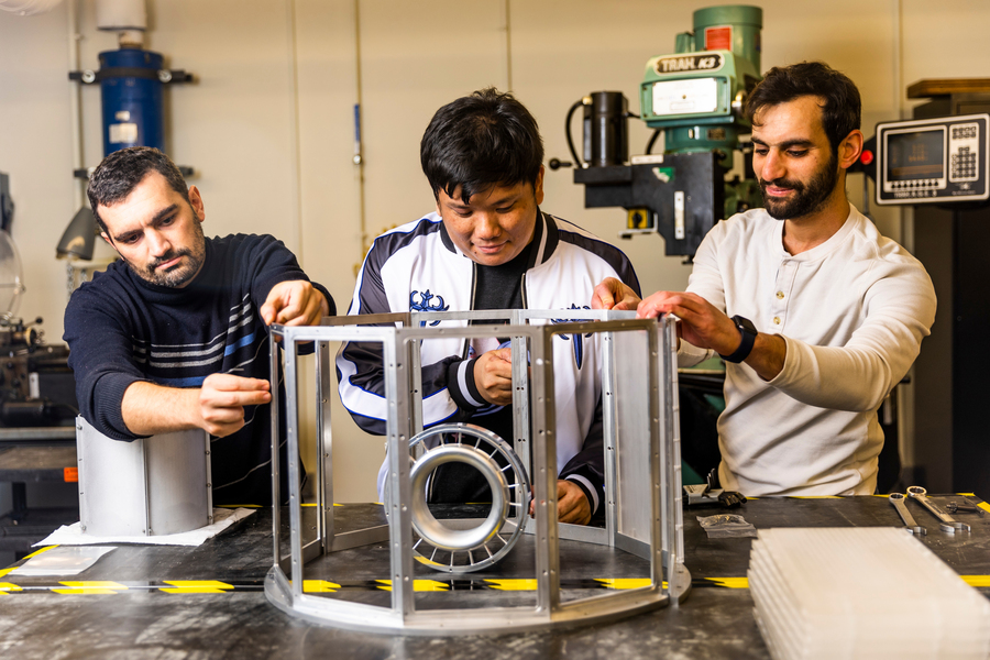 Three men working on a piece of hardware in a lab.