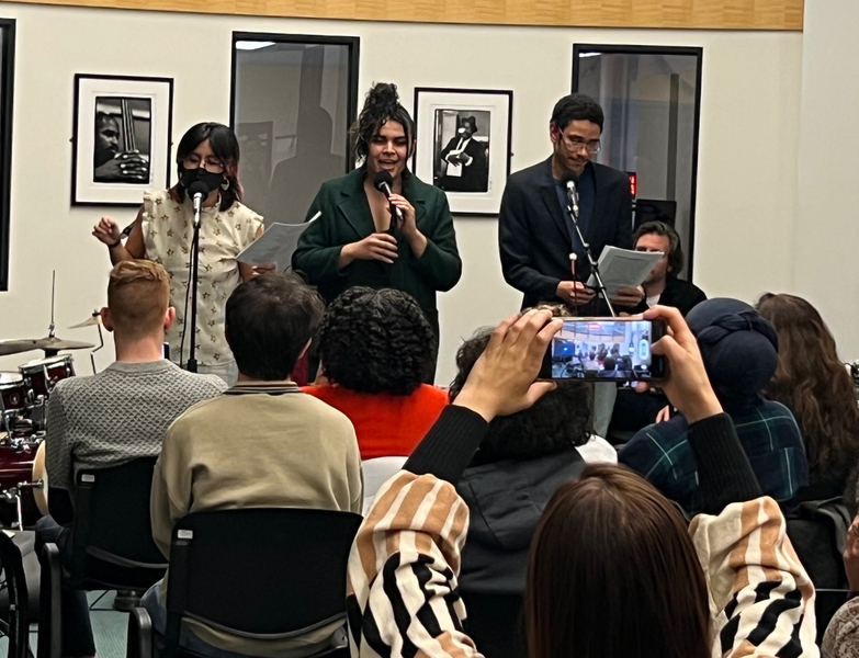 Dasha Castillo, Allessandre Santos, and Ygor Moura stand in a white room with microphones in front of an audience
