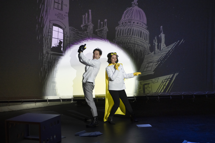 Aaron Engebreth as Charles Babbage and Aliana de la Guardia as Ada Lovelace strike an exaggerated pose as crime fighters on stage in the spotlight