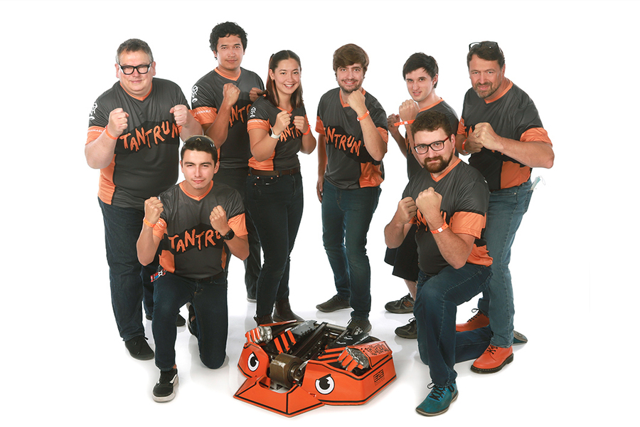 The Tantrum team poses with their fists in a fighting stance with their orange and black robot in the center. They are wearing orange and gray shirts with "Tantrum" printed on them.