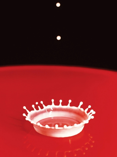 A drop of milk splashes against a red table forming the shape of a crown.