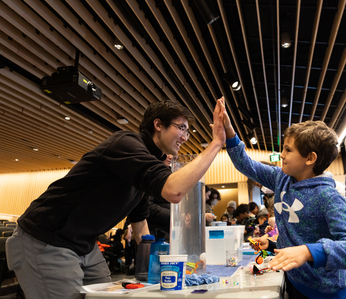 A graduate student and child high-five across a table; water and craft materials in the background