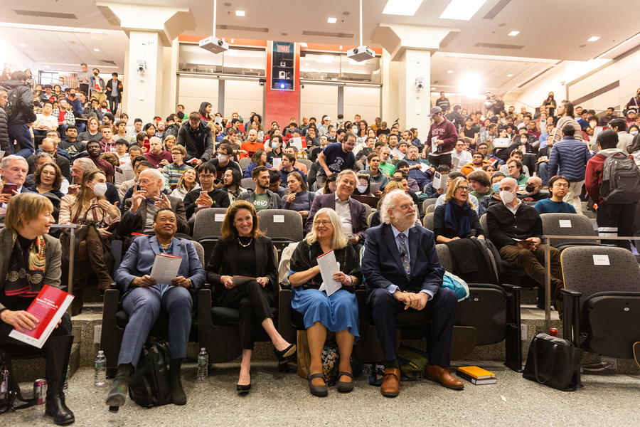 Photo of the audience in a large lecture hall. All the seats are filled, and people are standing at the back.