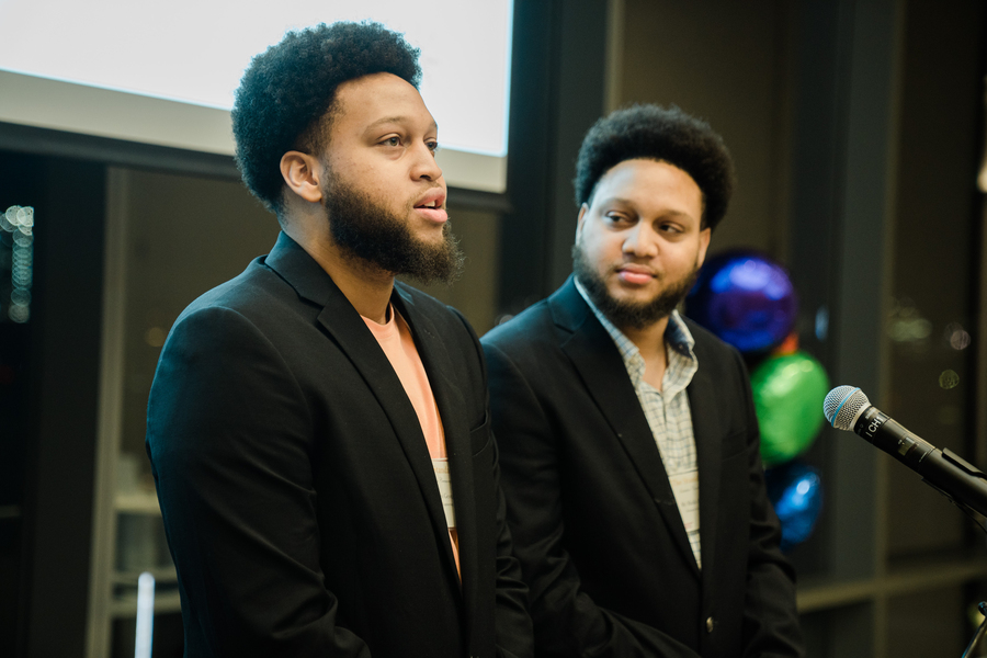 Photo of twin brothers Miles and Malik George standing before a microphone