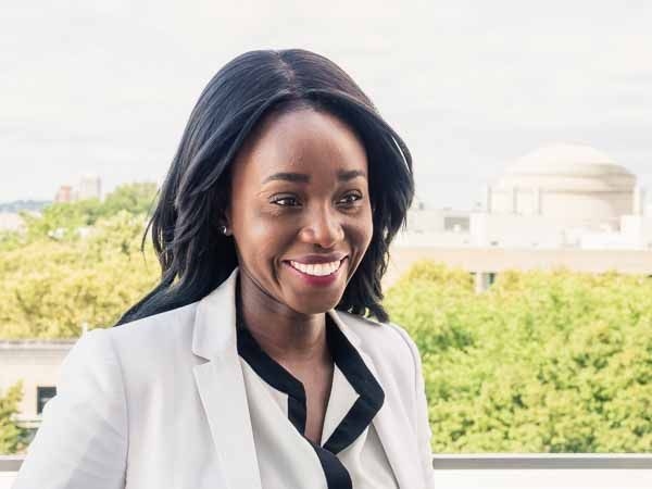 Ezinne Uzo-Okoro is pictured outside, smiling and gazing off to the right. Green trees and the MIT dome are in the background