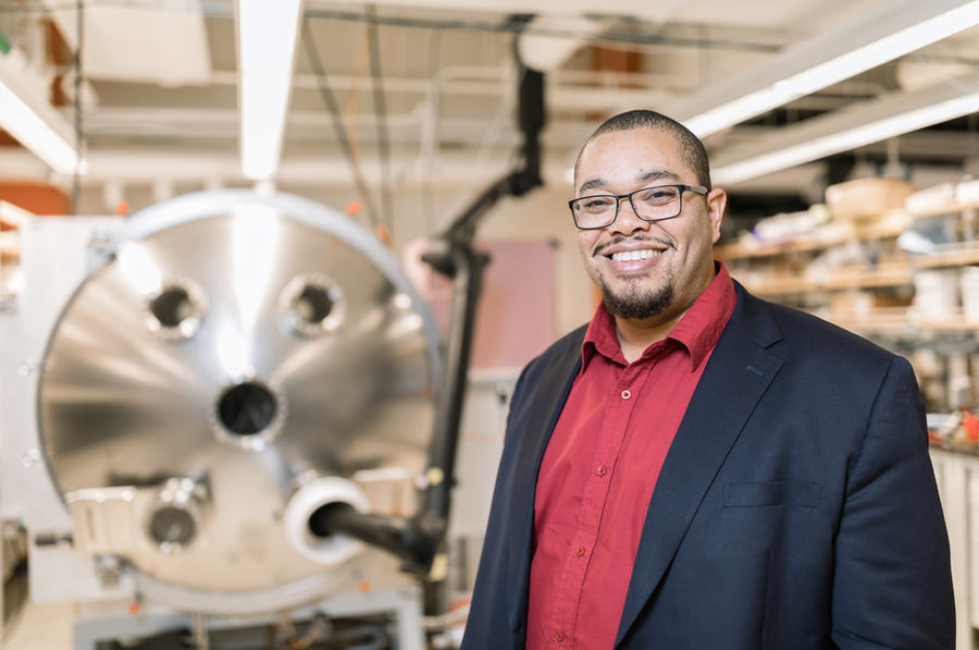 Asegun Henry poses in a lab before a large spherical metallic machine