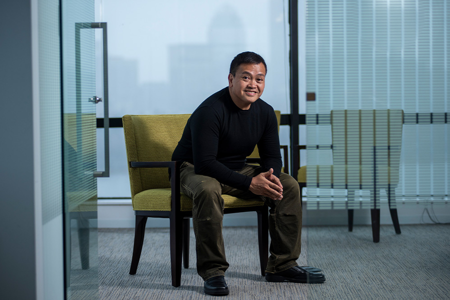 Leo Anthony Celi sits perched on the edge of an office chair, in front of a glass wall looking out onto other city buildings.