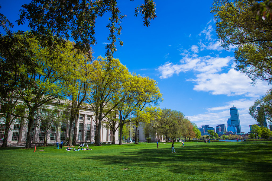 A sunny day in Kilian Court. Groups of friends relax on the lawn or play frisbee. In the distance is the Boston skyline.