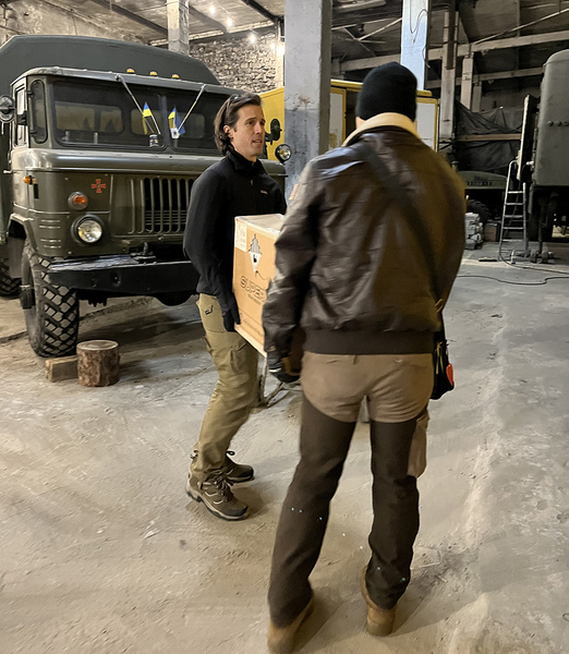Ian Miller and Mark Lindquist carry a box past a military truck inside a garage