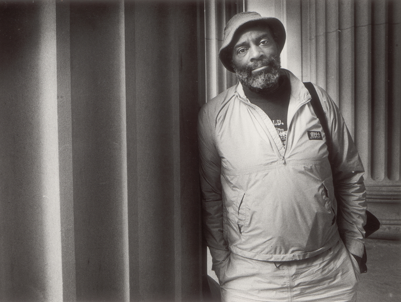 Black and white photo of Mel King leaning against large stone columns on the MIT campus
