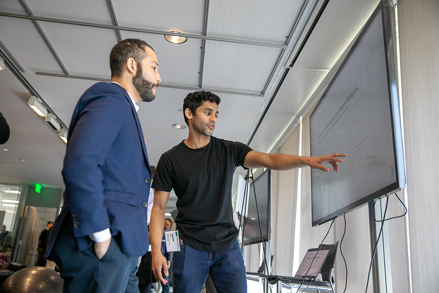 Photo of Sayash Fullay pointing to a large screen while explaining his research to someone else.