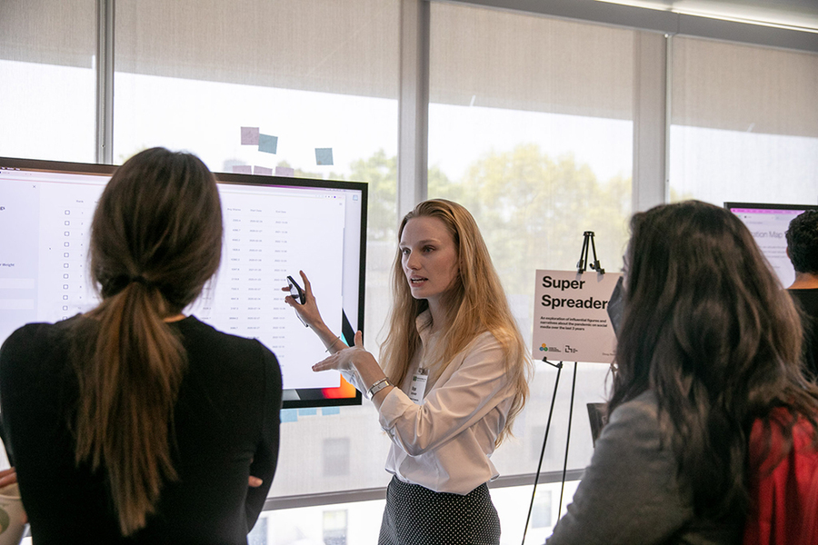 Photo of Hope Schroeder pointing out data on a large screen to two others whose backs face the camera.