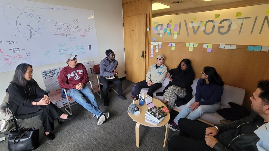 Seven people sit around a small table, talking