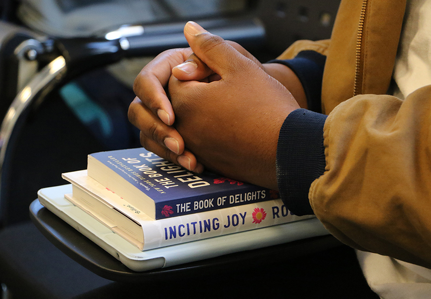 Closeup of folded hands resting on two books of poetry.