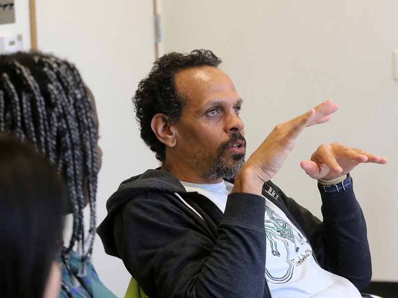 Poet Ross Gay gestures to students while speaking in a classroom