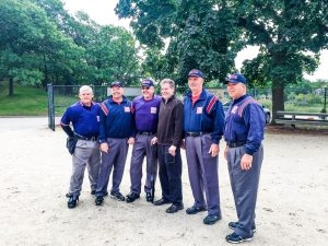 Six men in umpiring uniforms stand together on a baseball field.