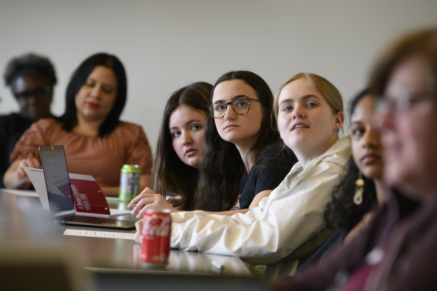 Seven people, including teens and adults, are seated at part of a large conference table. Several are looking up in the same direction.