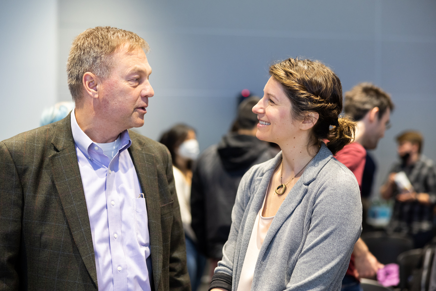 Mike Belding and Laur Hesse Fisher stand facing one another, smiling and talking, in a large room where others are milling about.