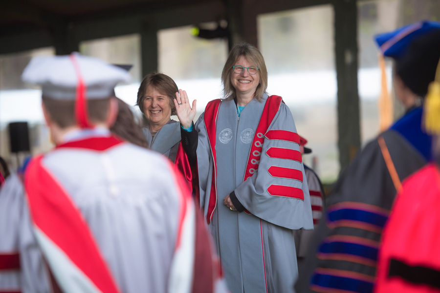 Sally Kornbluth waves as guests wearing ceremonial academic regalia enter the tent.