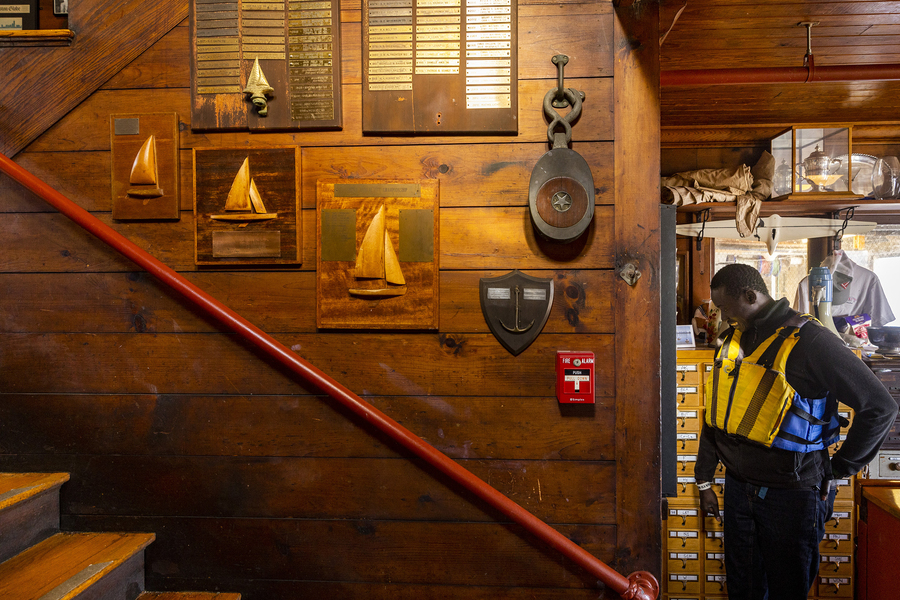 A community member wearing a life jacket looks at memorabilia. A staircase leads up.