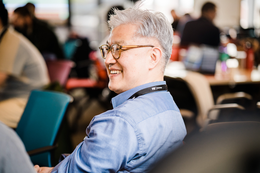 Photo of a man sitting in an office chair, smiling at a discussion happening off screen.