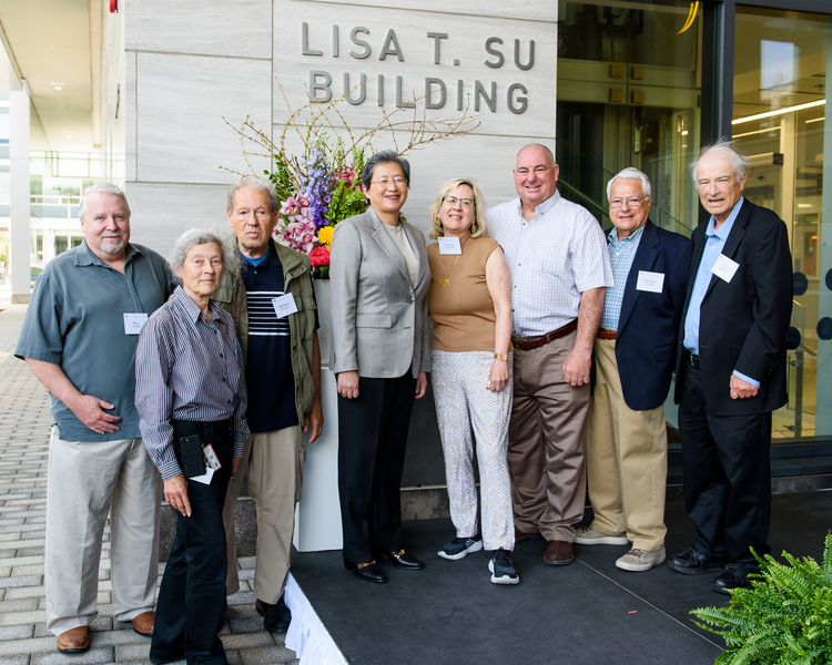 8 people stand together alongside a building with a sign that reads "Lisa T. Su Building"