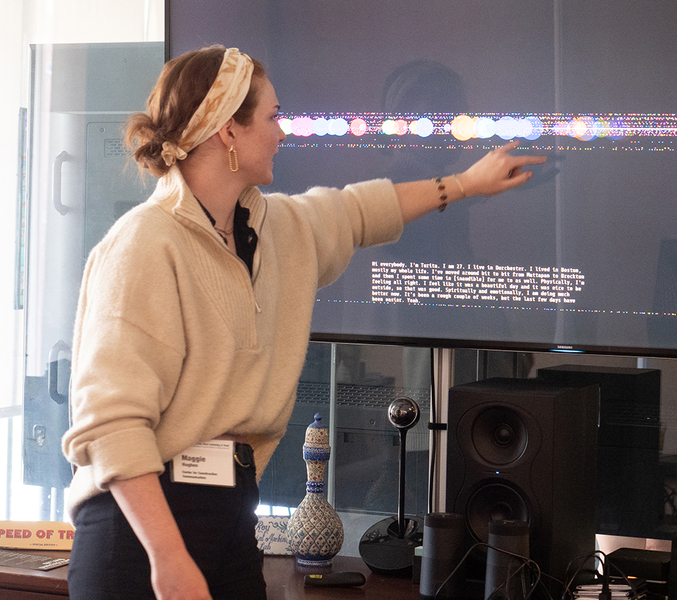 Maggie Hughes points to a row of circular data visualizations on a large screen, while explaining her research findings.