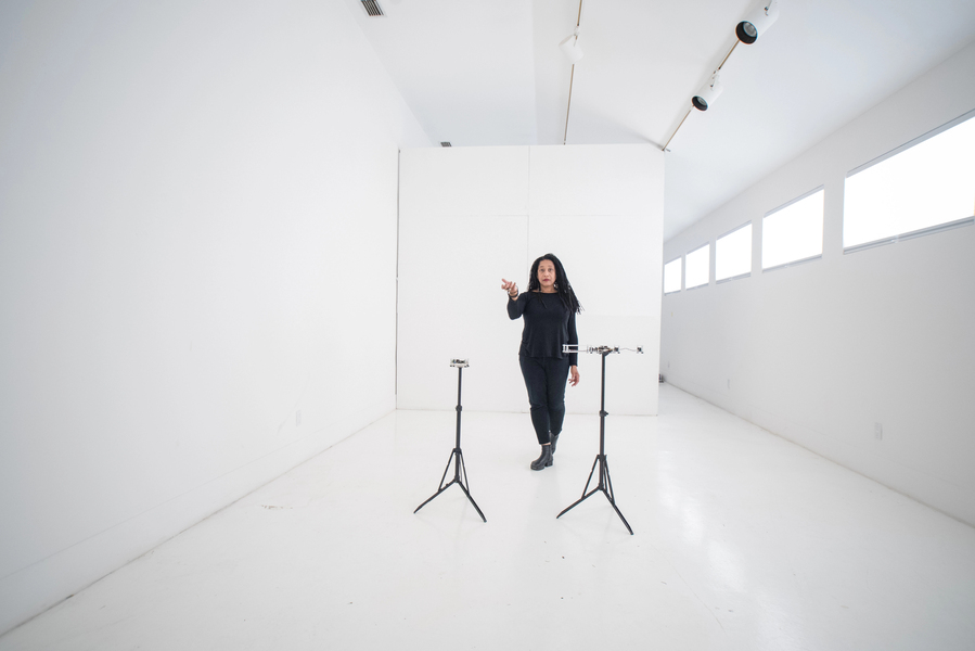 Pamela Z in a bare white room in front of electronic instruments