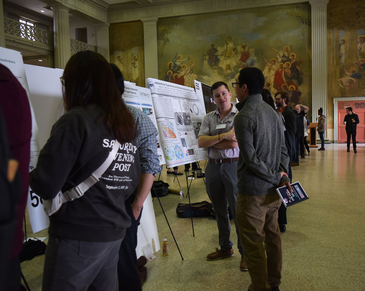 Several people peruse and discuss a row of posters