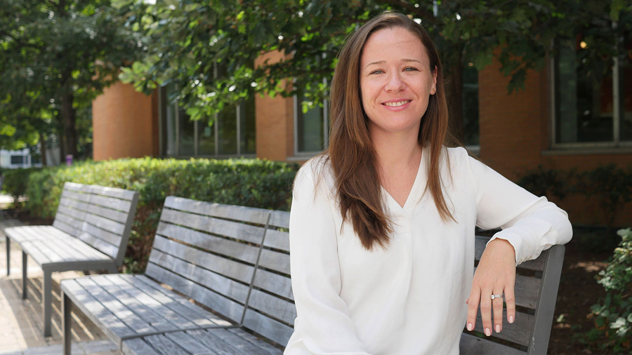 Sara Prescott sitting on an outdoor bench in front of some trees on a sunny day