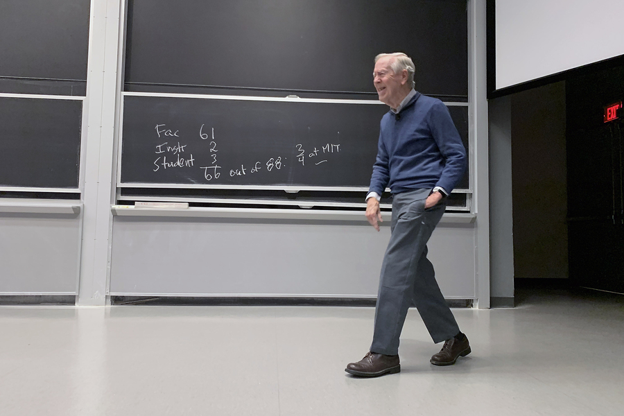 Gil Strang strides in front of a chalkboard, smiling. On the board is a simple math equation: 66 + 2 + 3 = 66 out of 88: 3/4 at MIT.