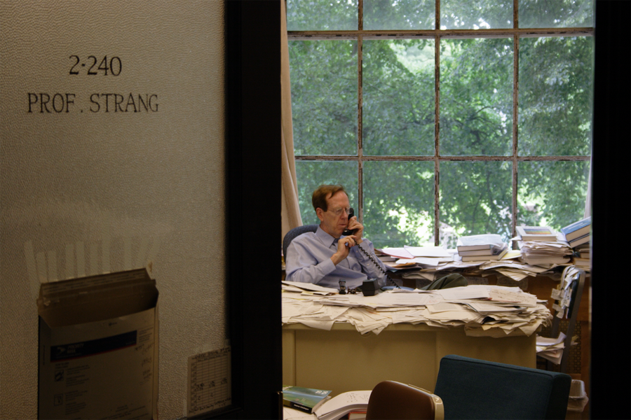 Gil Strang in middle age sits at his office desk, talking on the landline telephone, surrounded by mounds of paper.