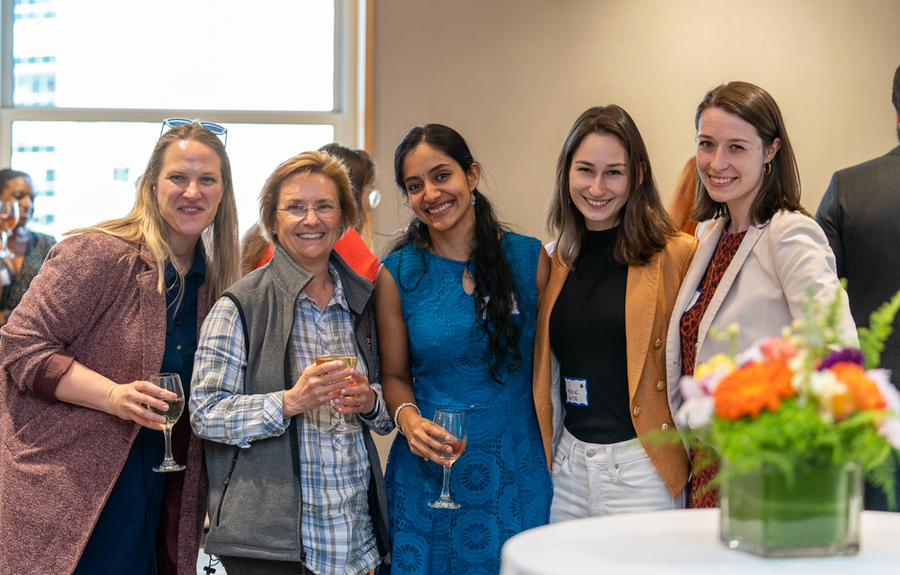 Five women stand together, posing for the camera in a crowded room