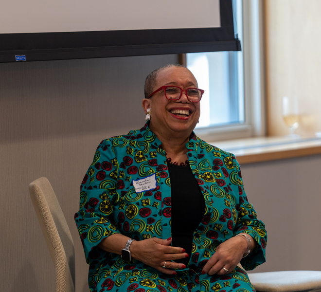 Dean Blanche Staton laughs while seated in front of a blank wall projector screen