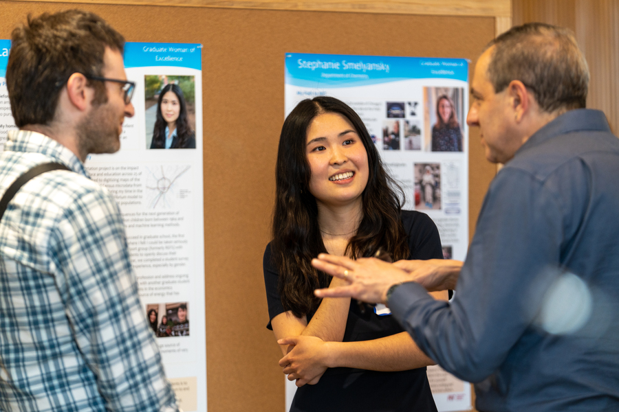 Two men speak with a woman graduate student in front of her poster