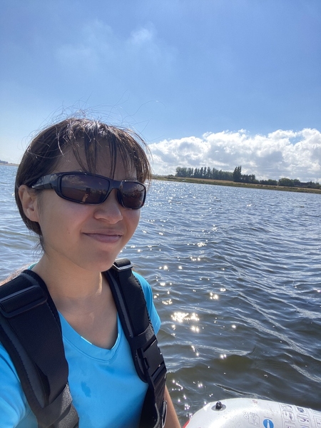 Andrea Lo selfie. She is seated in a small boat with a grassy area off in the distance.
