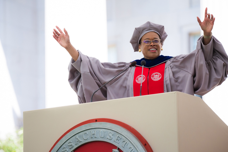 Chancellor Melissa Nobles in academic regalia speaking at a podium with her arms raised