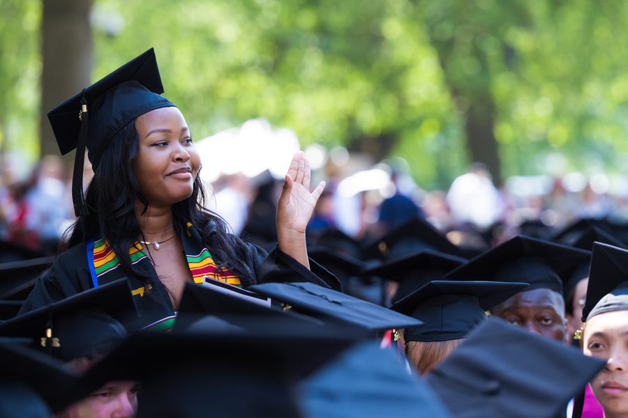 A female graduate standing above the black mortarboard hats of her seated fellow graduates.