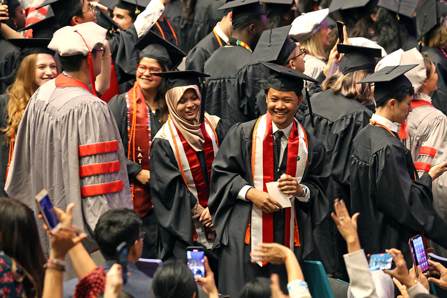 Men and women in academic regalia in a crowd, with loved ones snapping pictures of them with their cellphones