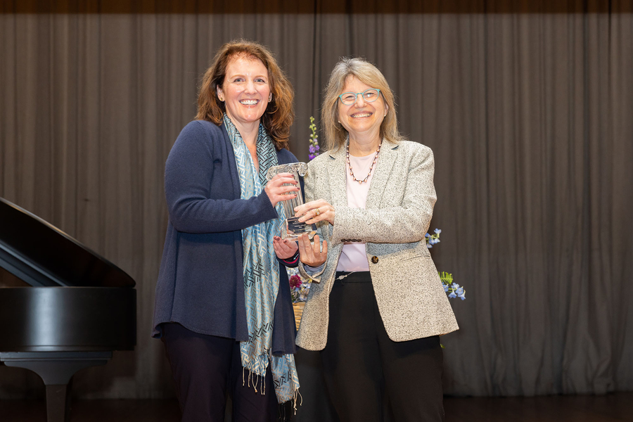 Kimberly Haberlin and Sally Kornbluth standing with a piano and flower arrangement behind them, holding a small statue of a glass column.