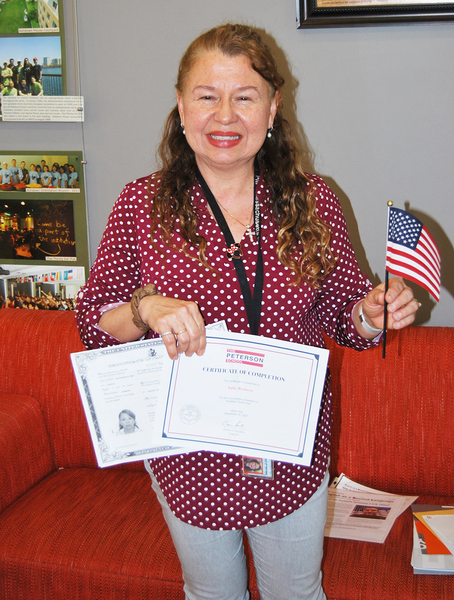 Photo of Sally Romero holding an American flag in one hand and two certificates in the other.