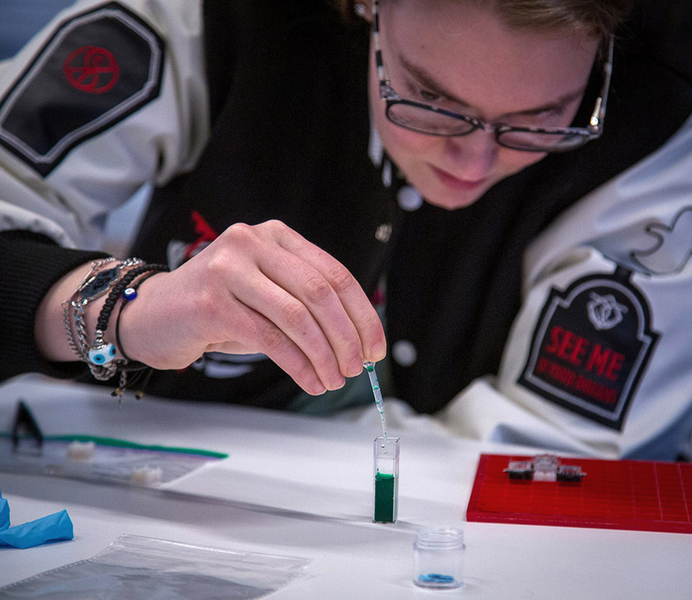 A student drops green food coloring into a small tube.