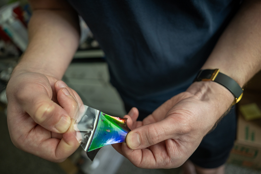 Two hands pulling a thin piece of colored film away from a clear backing